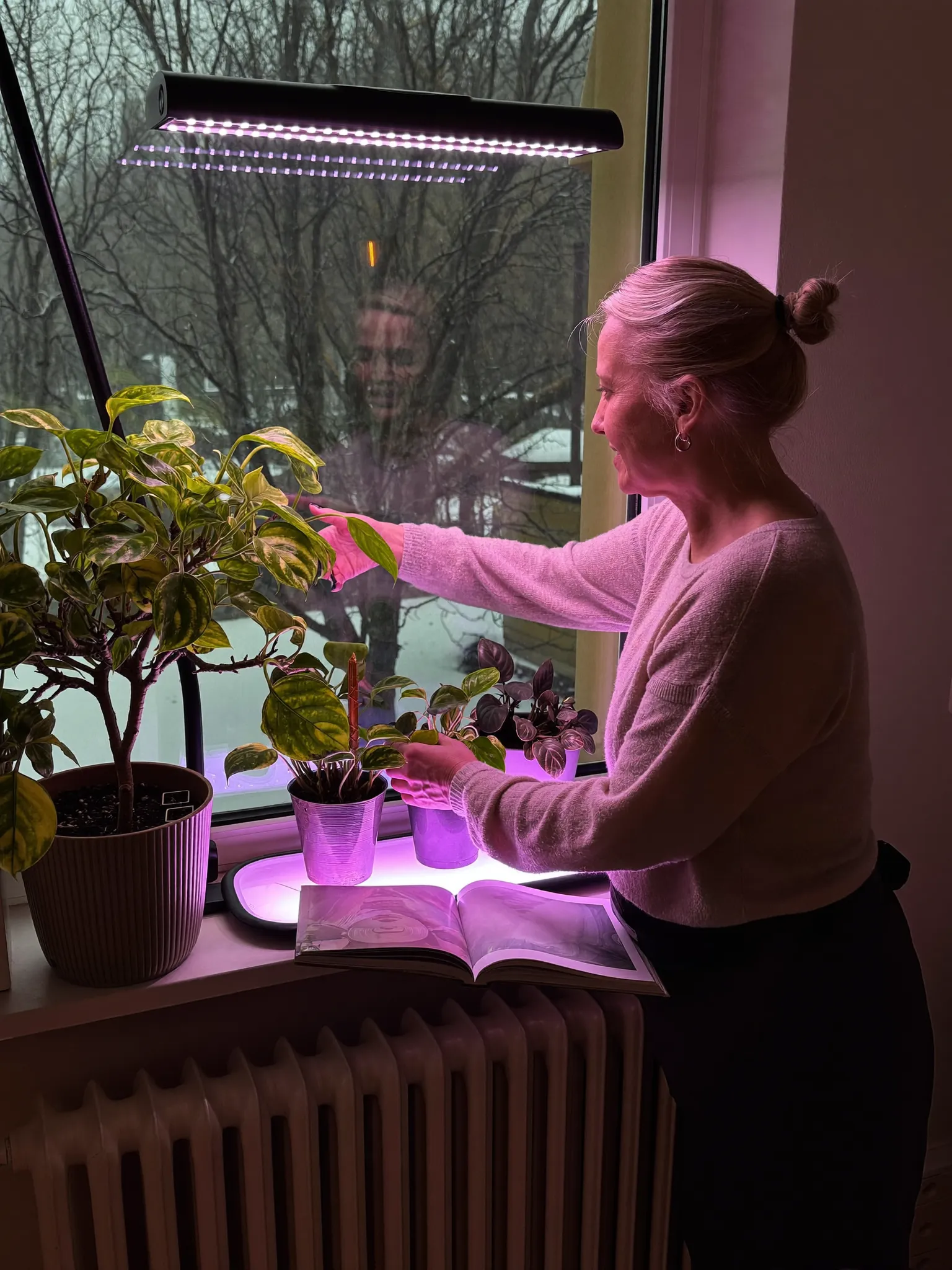 Ingrid tending plants under grow lights by a snowy Oslo window